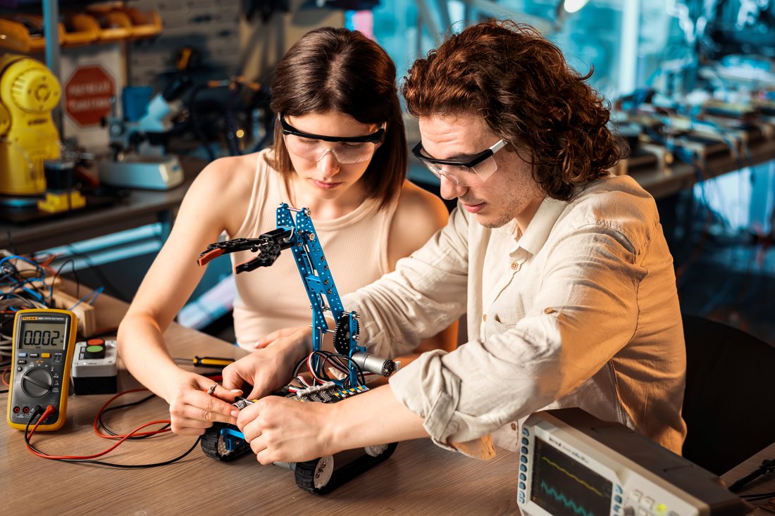 Studentka i student w okularach ochronnych budują ramię robota w pracowni